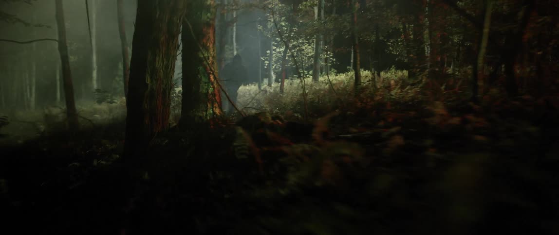 A man is running quickly through a forest at night with a spotlight following