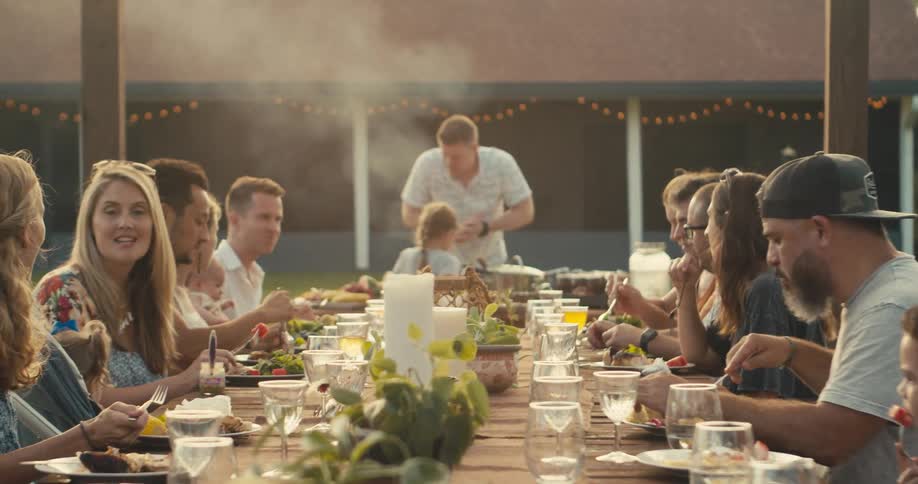 A group of friends sitting at long table eating and drinkinghas barbecue in the garden