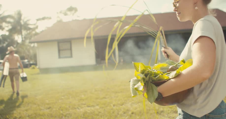 A woman picks weeds in her yard as a man walks off with a ladder
