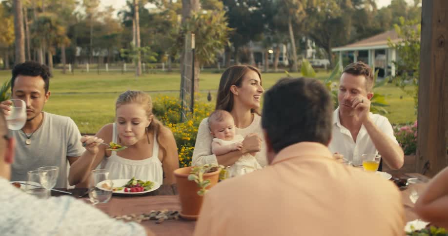 Friends and family eat lunch at a table in a park