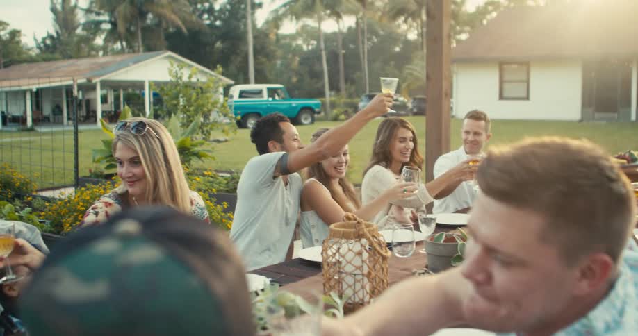 A family group sitting at an outdoor dining table toasts and clinks glasses