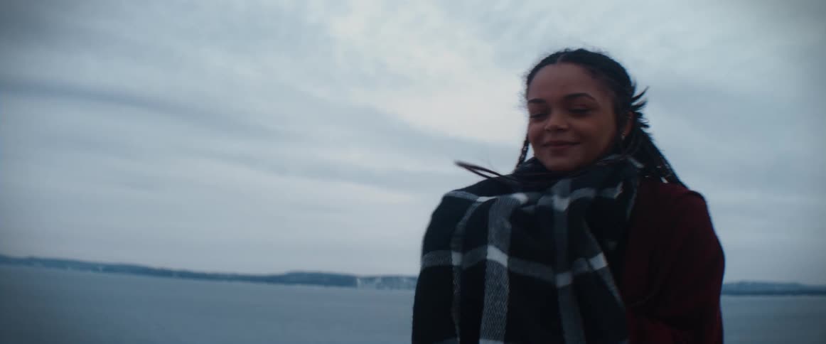 Woman with braids scarf and coat smiles and looks around on the coast on a cloudy cold winter day