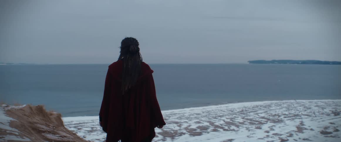 A woman walks to the edge of a cliff overlooking the sea