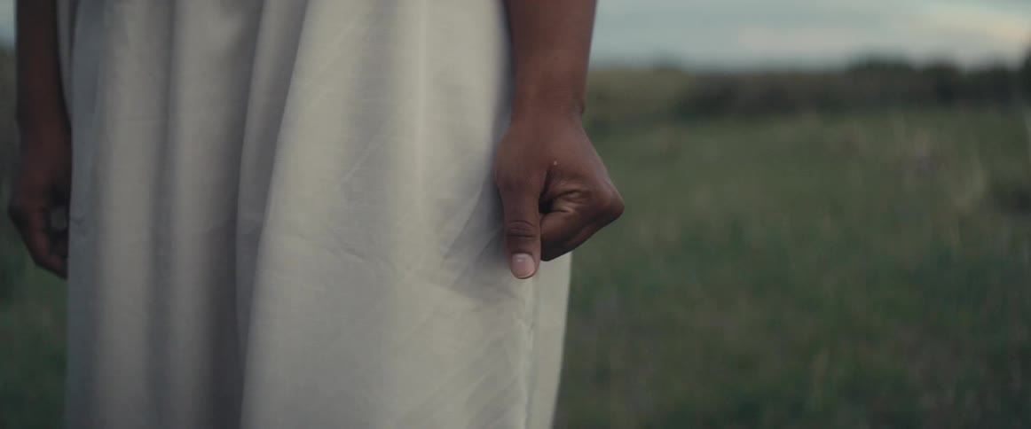 Woman with white dress clenches fist in the field