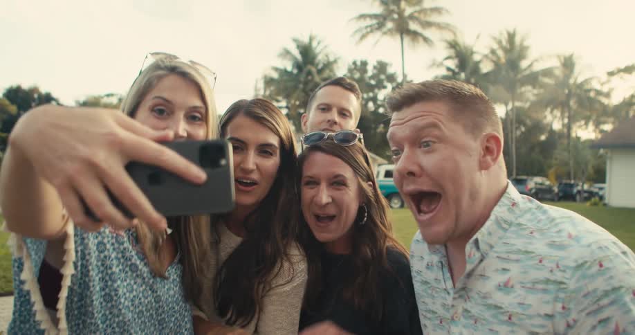 A woman holds her cell phone for some men and women to look at and then they all cheer and clap and yell