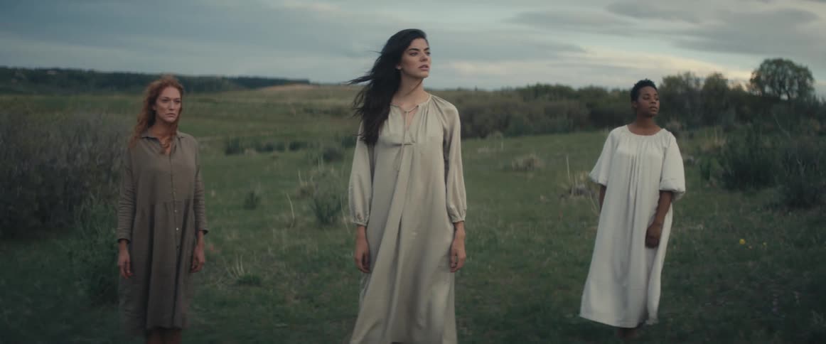 Three women stand on the field together on a windy day