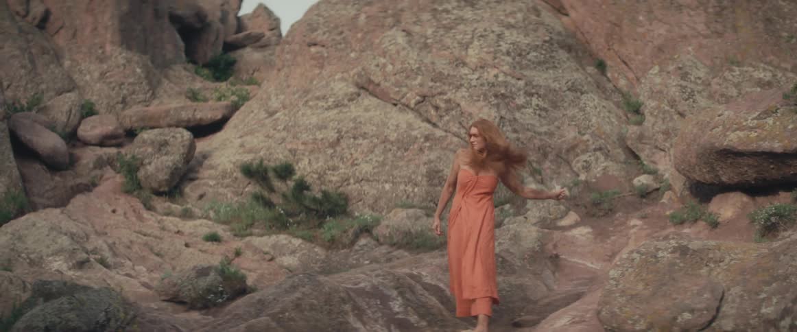A redheaded woman picks up sand from the side of a canyon and throws it aggressively