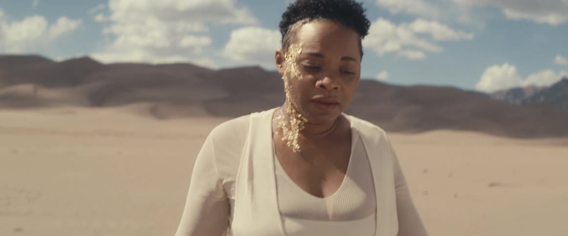 A woman walking in the desert with gold leaf makeup decorating half of her face