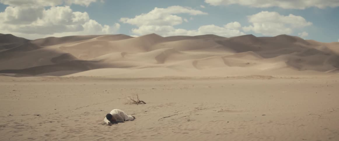 A man lies motionless in the sands of desert during the day