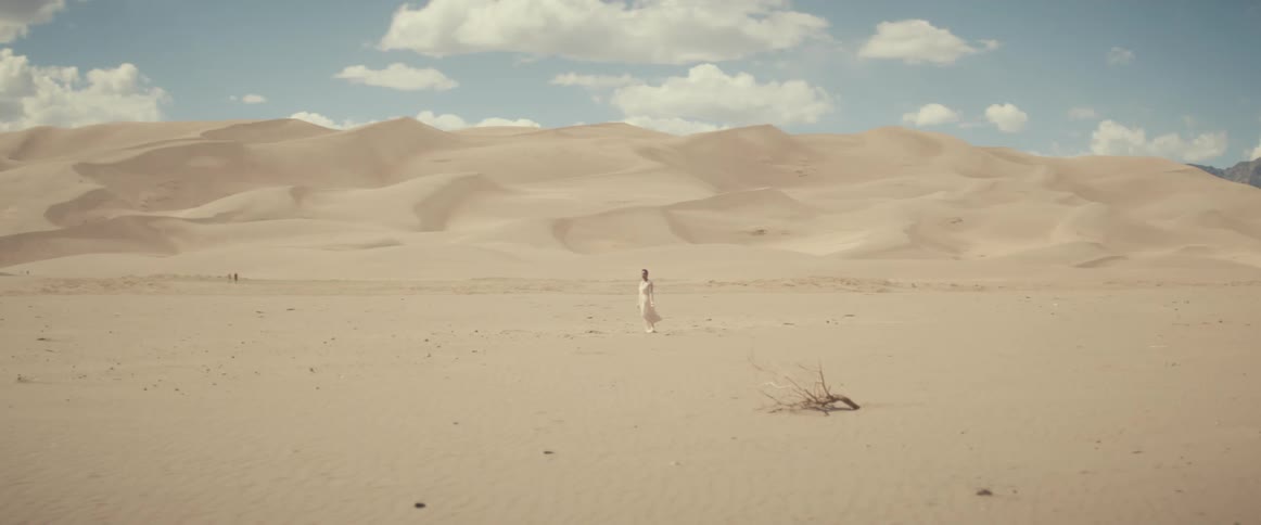 A woman stands in the desert in a white dress