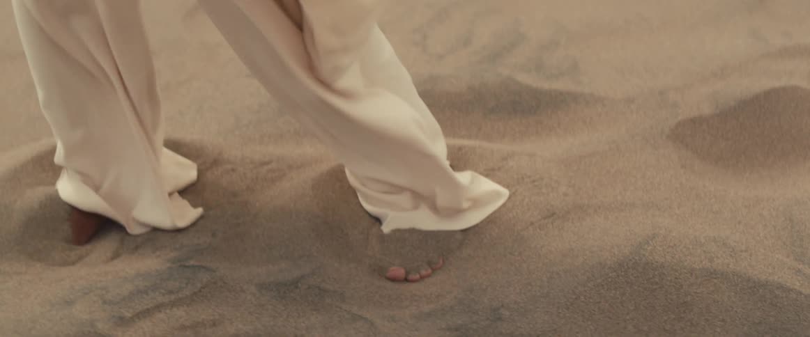 Woman wearing white dress stands in white sand desert
