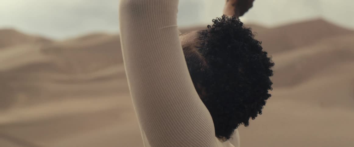 A woman looks around and reaches her arms up while standing in the desert