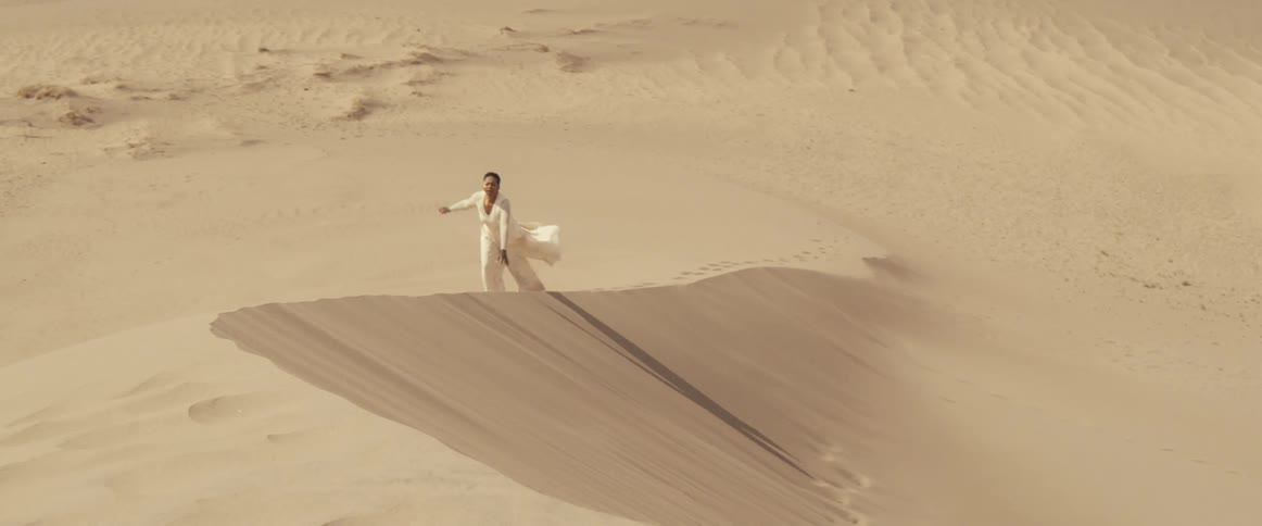 Woman with short hair and white dress climbs sand dune in desert