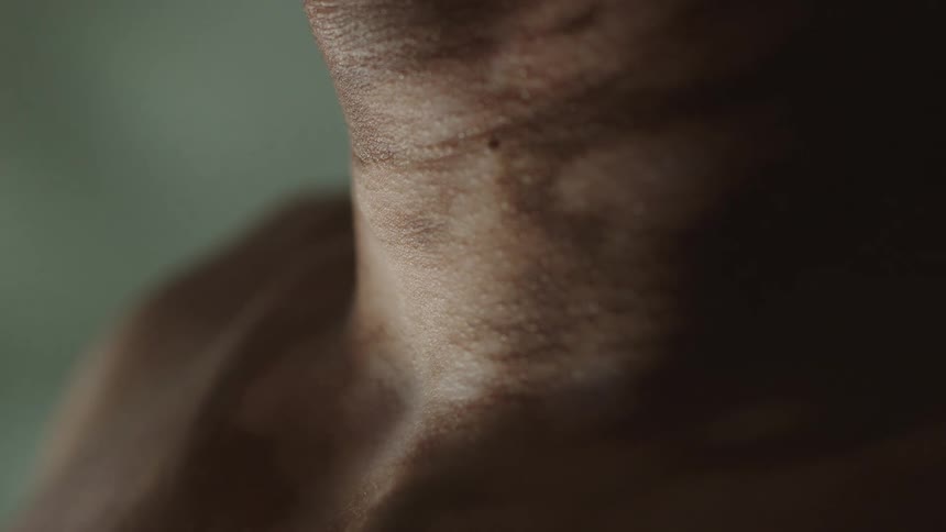 A man with a tattoo stands upright and swallows which is shown on his throat