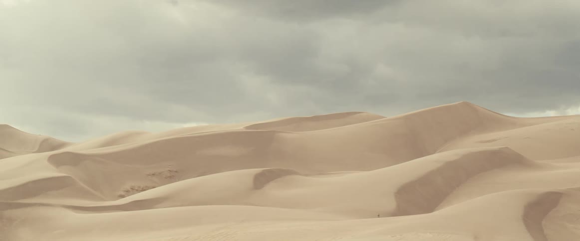 View of sand dunes in desert under clouds