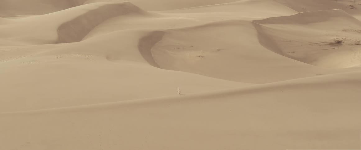 Distant woman with white dress stands on white sand in the desert