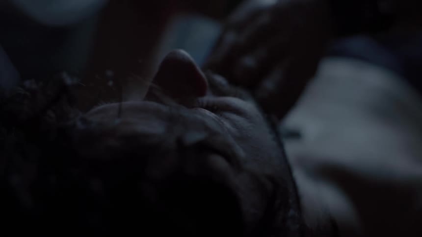 A man rubs his face with his hands while resting in a dimly lit room