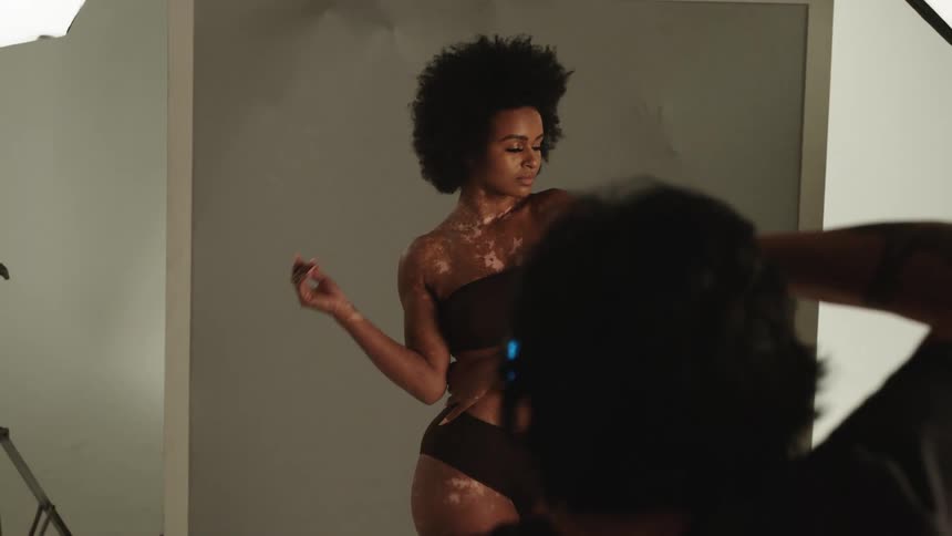 A woman is having her photograph taken in front of a wall with hands poking through