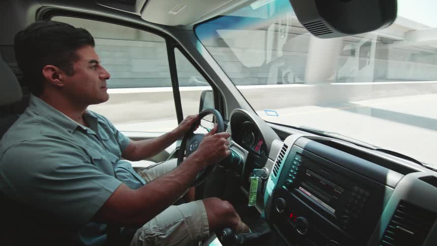 Worker drives a black transport van through the highway in the city at morning