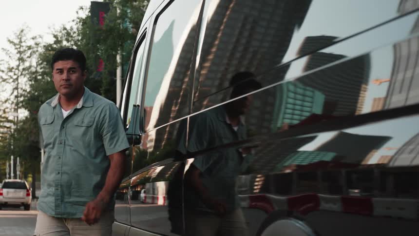 Focused male worker steps out of a black transport van parked on a downtown city street
