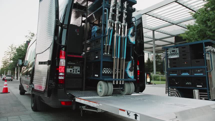 A large piece of equipment is rolled onto a lift on the back of a van