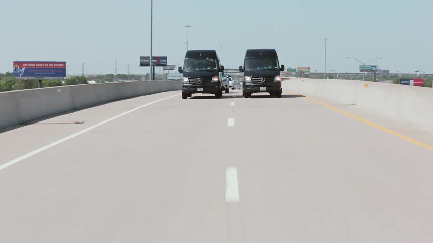 Two black vans are side by side on a freeway holding up other traffic