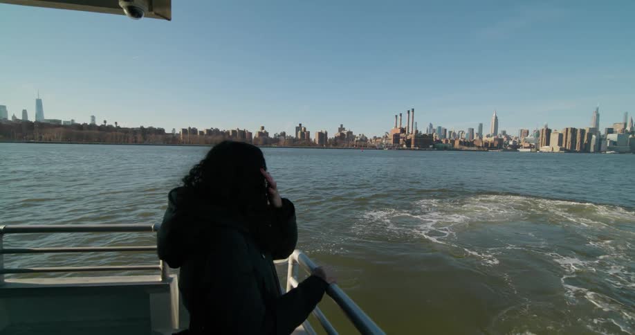 A woman on a boat looks out at the river and the city skyline in the distance