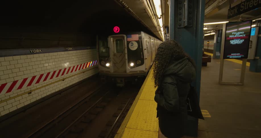 A woman stands on a train track as a train with people on it pulls up