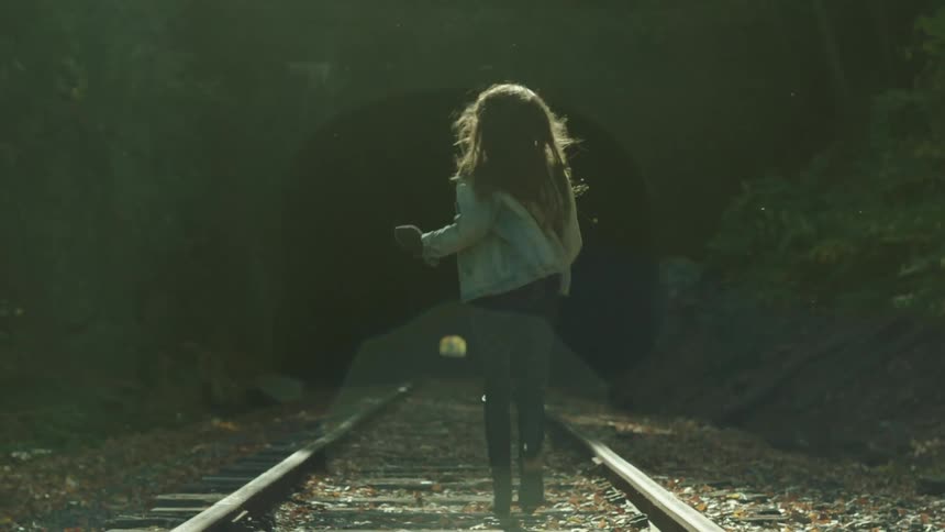 A woman is running towards a dark tunnel on train tracks