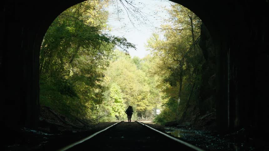 Two people running along train tracks and headed into a tunnel