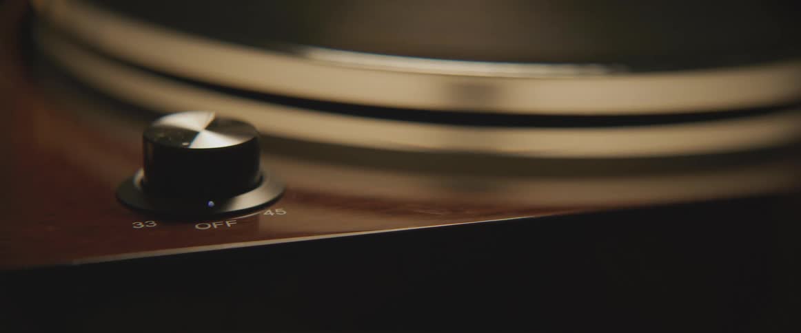 Person turns the on off knob on a vintage turntable inside a dimly lit room