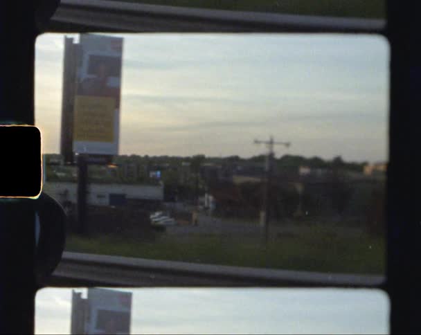 Footage of a small town filmed from a moving vehicle at sunset caught on vintage film