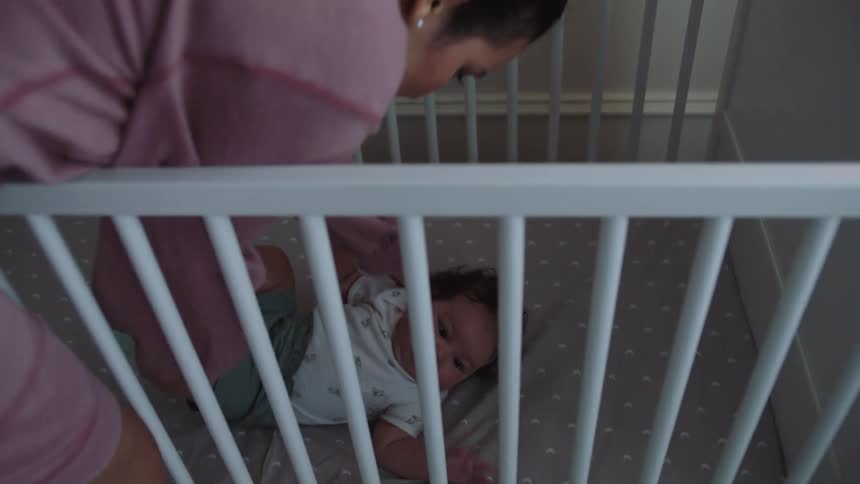 A mother puts her daughter to bed in the crib