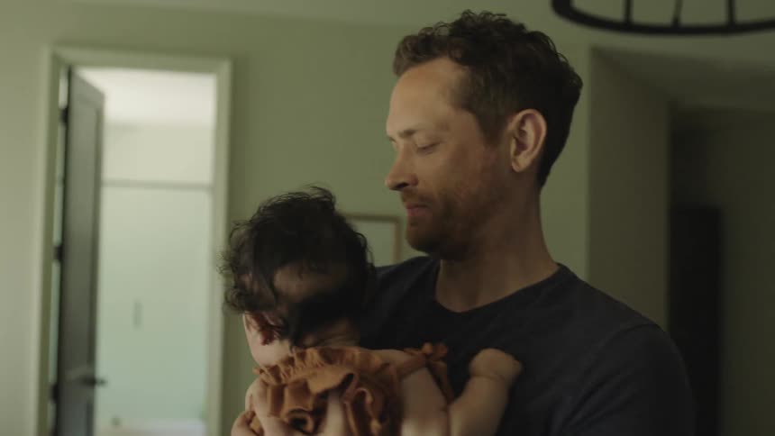 A man picks up the baby as the woman is making the bed