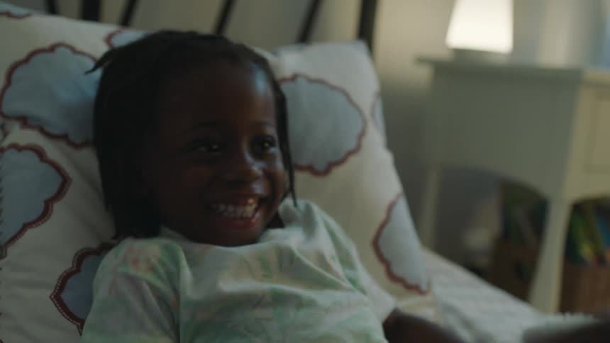 Small child laughs while being tickled in bed at home