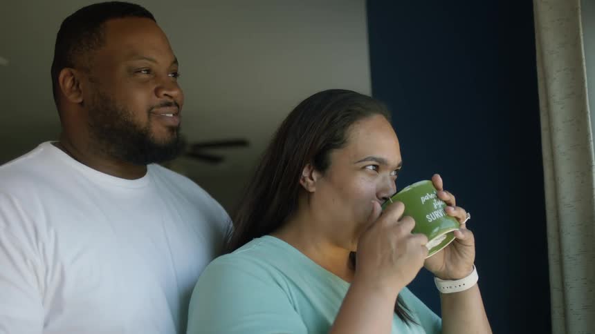 A husband kisses a woman drinking coffee at home