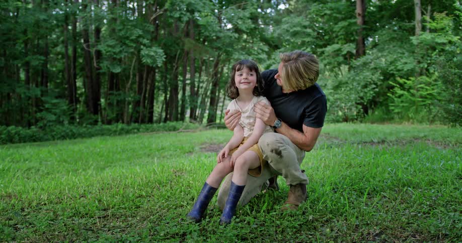 Father and daughter hugging while kneeling over the green grass near the forest