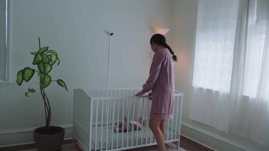 A woman is standing over a crib looking at a baby