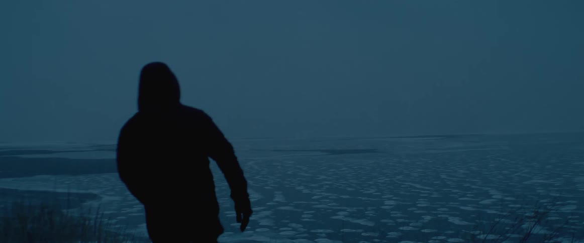 Silhouette of a man wearing winter clothes walking towards the frozen ocean at night