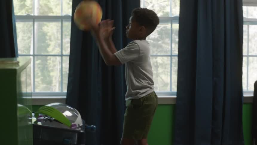 A boy is bouncing a ball around his bedroom