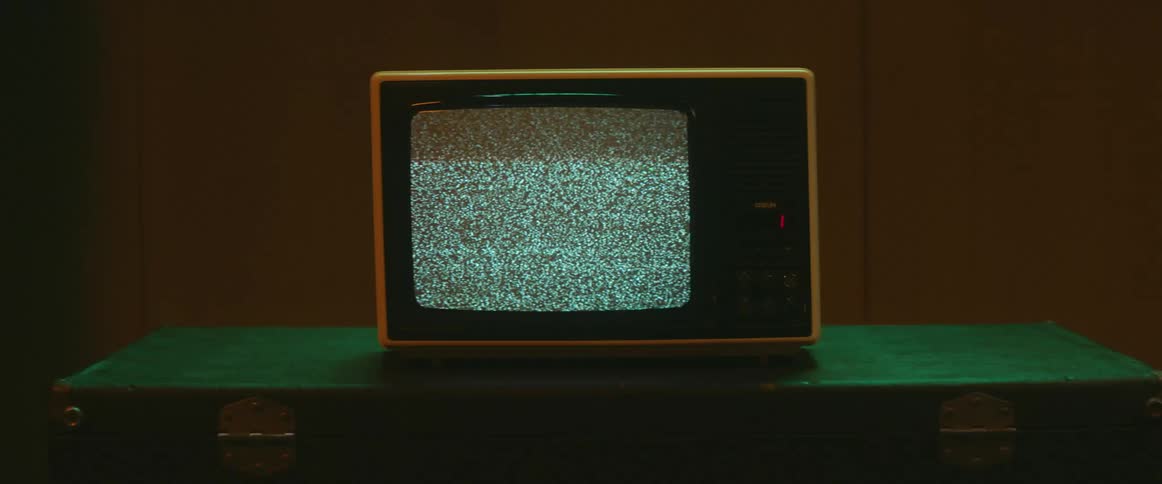 Static and white noise on the screen of a vintage television over a table inside a room