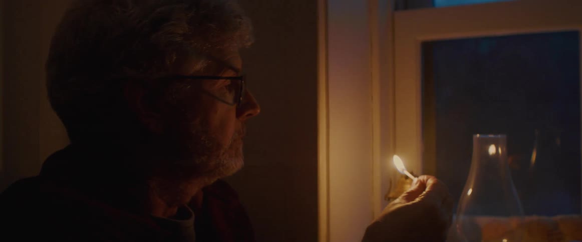 Man inside a dark room in a house light a gas lamp with a match
