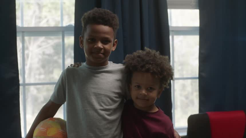 Siblings stand with their arms around each other posing in bedroom