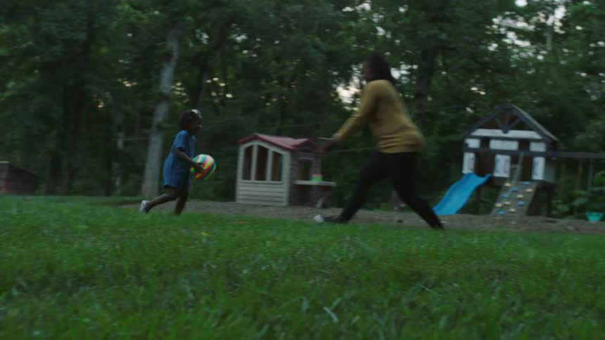 A mother and daughter toss a ball around the yard