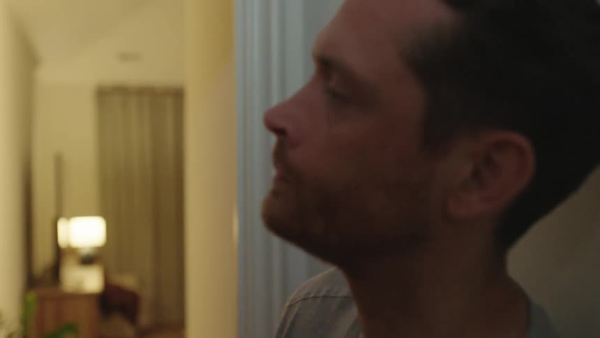 A man looks stressed as he rubs his neck then walks into a room