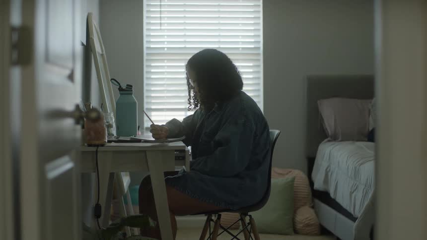 A girl is doing homework at a desk in a bedroom