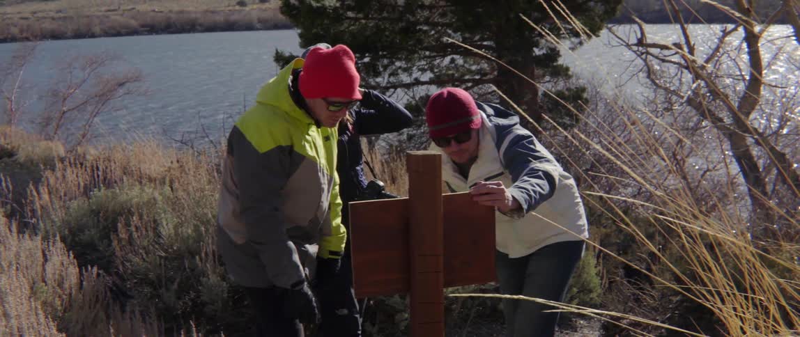Three people examine a signpost in a setting near a body of water