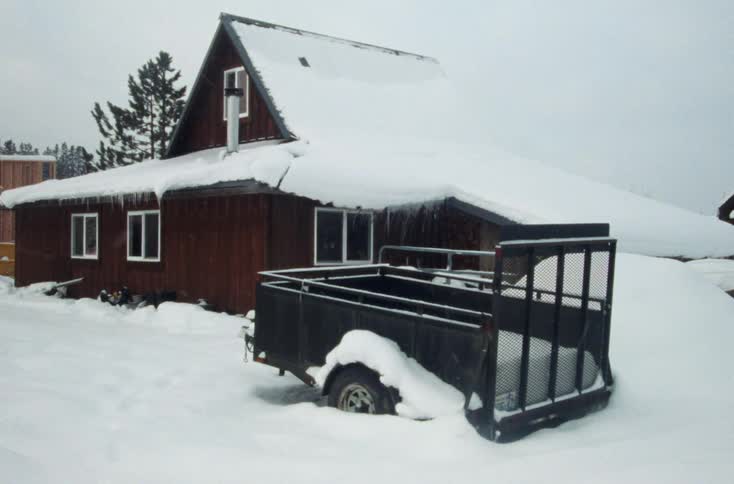 Snow falling over a horse transport carriage parked in front of a house in the countryside