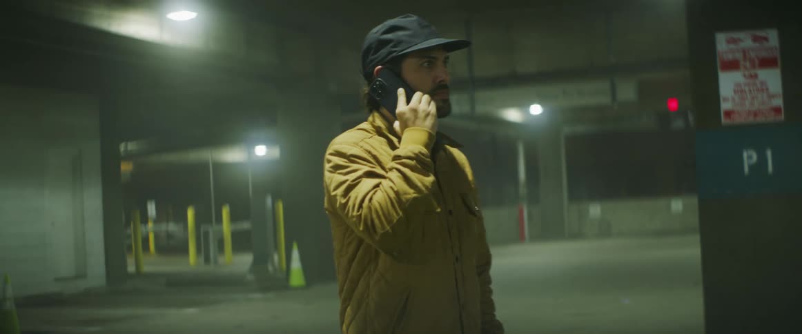 A man in a yellow jacket paces while talking on his cell phone
