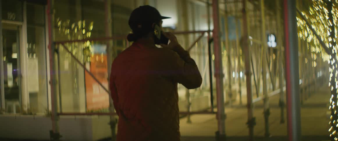 A man holds his smartphone to his ear as he walks through a city at night